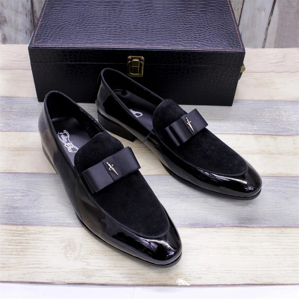 Men's black tassel loafers with matte and glossy patent leather uppers and a rubber sole, shown on a wooden surface.