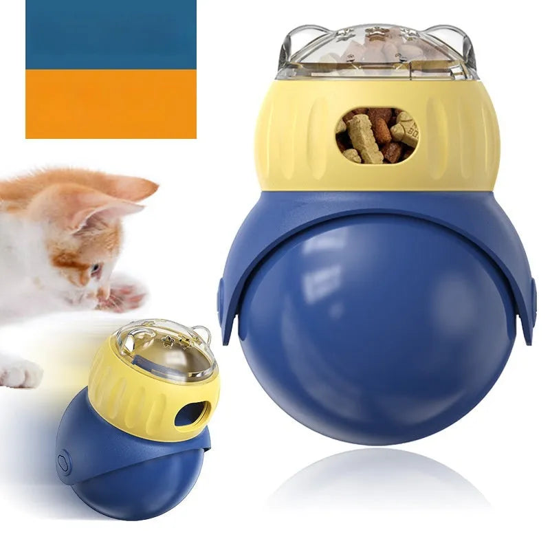 Yellow and blue owl-shaped plastic tumbler toy for cats, a slow-feeder puzzle on a wooden floor.