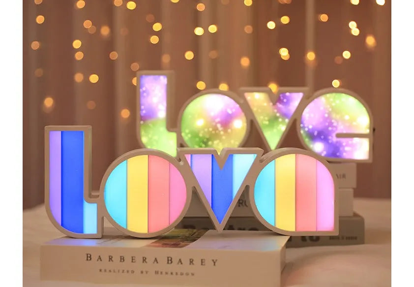 Rainbow-coloured LED LOVE decorative lamp with plastic shell on a table.