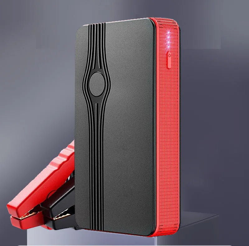 Red K4-E portable car jump starter and power bank unit with USB cable on a table.