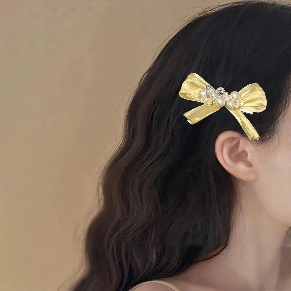 Yellow bow hair barrette with rhinestone and pearl details on duckbill clip