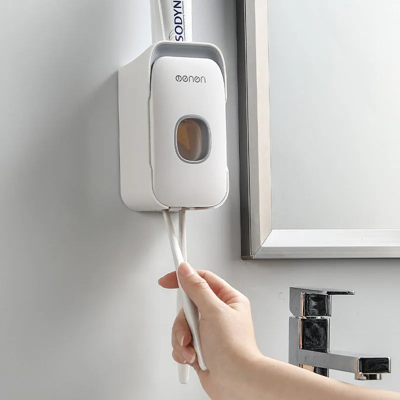 Automatic toothpaste dispenser in grey, blue, and pink colours on a bathroom countertop.