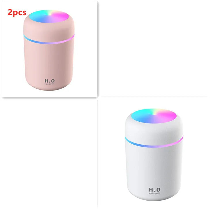 Pink USB mini humidifier with LED lights on wooden desk beside laptop