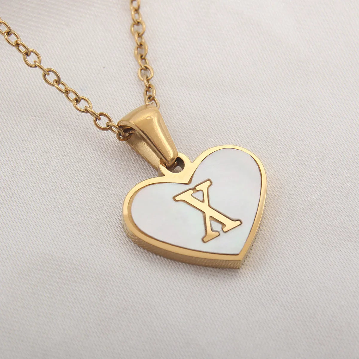 Gold-plated heart necklace with white shell pendant showing initial engraving on stainless steel chain