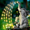 A textured resin elephant garden statue with a built-in LED light strip illuminating its back, placed amongst plants.
