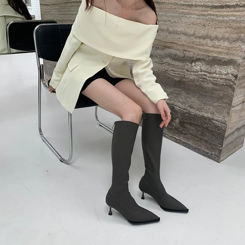 Black pointed toe below-the-knee women's boots with a stiletto heel and a visible back zipper on a plain background.