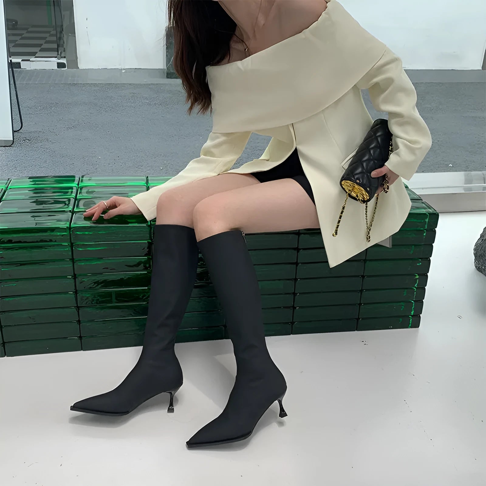 Black pointed toe below-the-knee women's boots with a stiletto heel and a visible back zipper on a plain background.