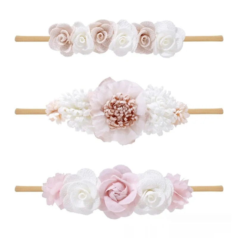 Three cloth flower-shaped hair bands for children in different styles on a light background