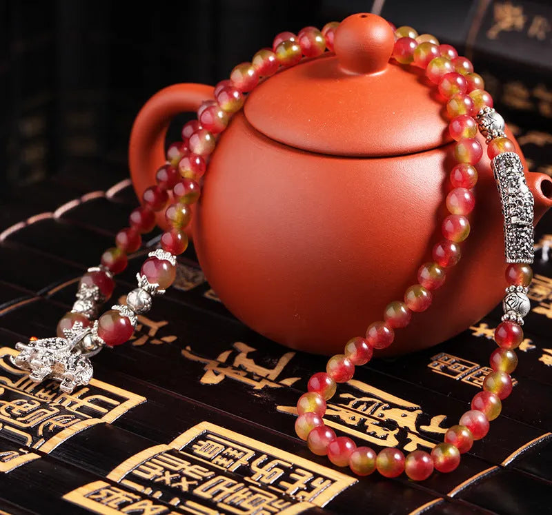 A handmade bracelet with geometrically cut watermelon crystal beads and a red Chinese knot closure on a white background.