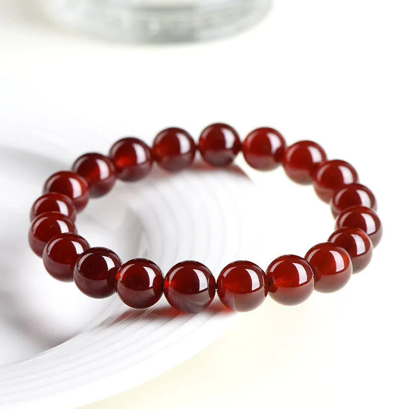 Natural orange red garnet crystal ball bracelet with a gold-toned Ruyi charm on a white background.