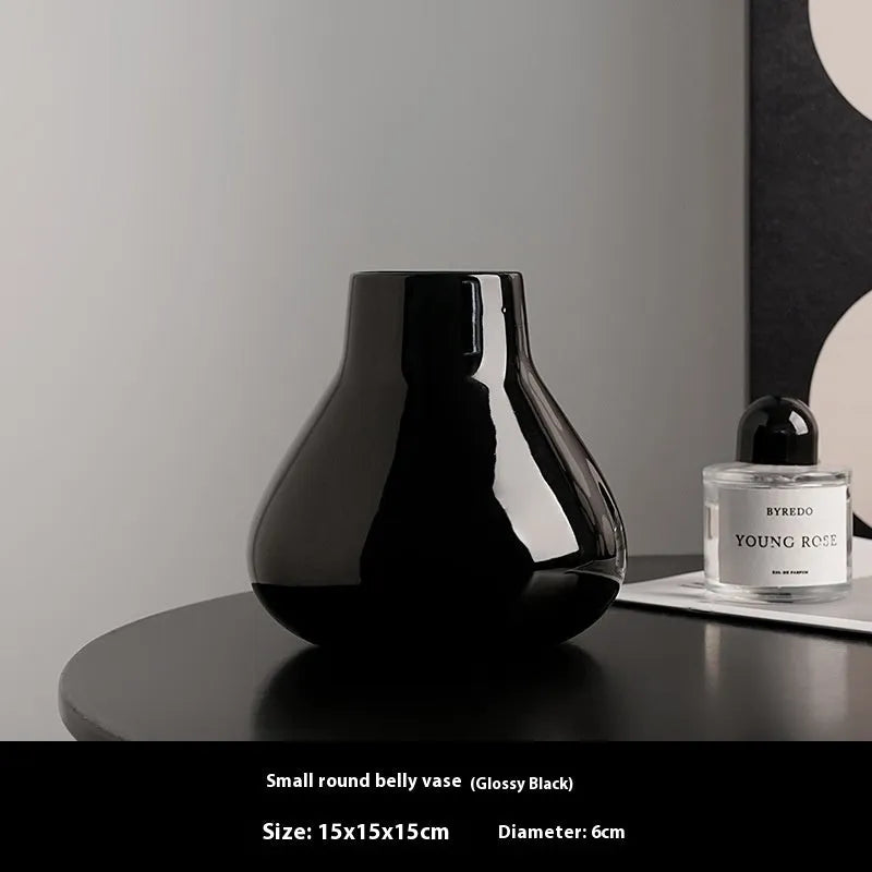 Modern round belly ceramic vase with coloured glaze, shown in black and white, some with artificial flowers.