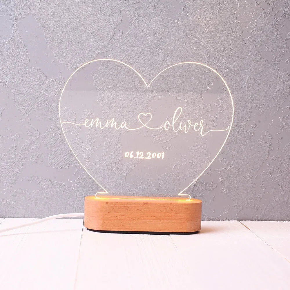 Custom transparent acrylic night light with engraved names and date, lit by an LED base on a table.