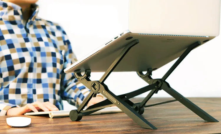 Black folding portable laptop stand with reinforced nylon construction shown unfolded beside laptop