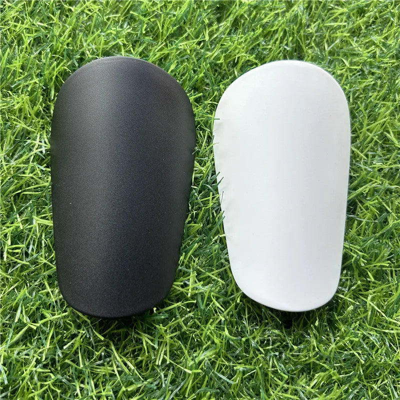 Extra small mini plastic football shin guards in black and white, shown at 8cm by 5cm size.