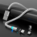 Magnetic charging cable with glowing LED light connected to a phone, showing black and silver colour options on a desk.