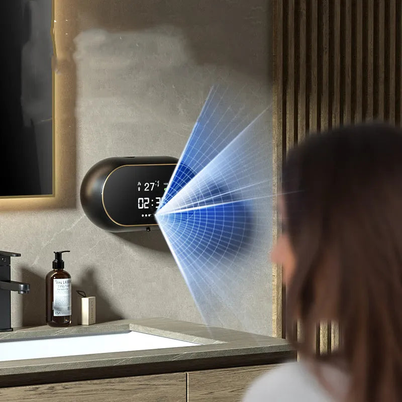 White automatic wall-mounted hand sanitiser dispenser with USB cable on a bathroom wall.