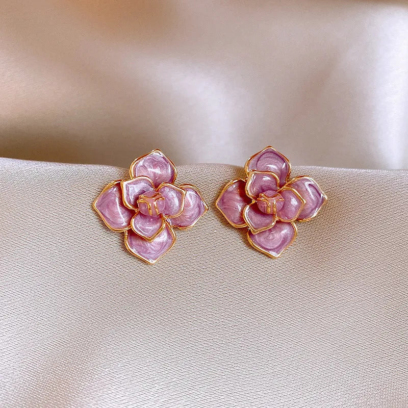 A pair of gold-plated purple flower stud earrings with a mottled oil-spot glaze on a copper base.
