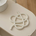 Irregular-shaped ceramic heat proof mat with hook and loop backing on a wooden table.