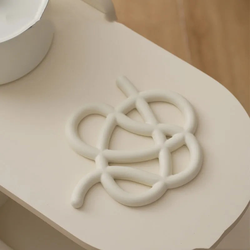 Irregular-shaped ceramic heat proof mat with hook and loop backing on a wooden table.