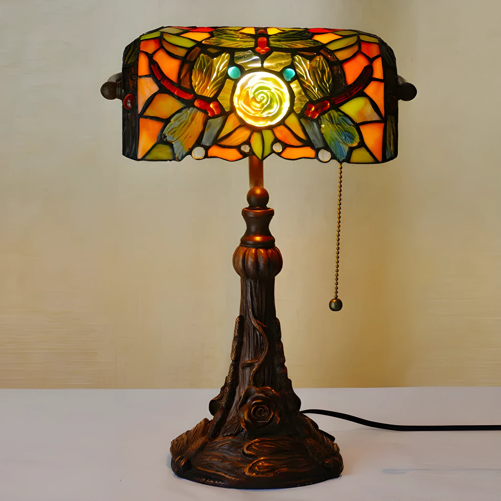 Tiffany style table lamp with colourful stained glass shade and resin base on a wooden table.