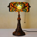 Tiffany style table lamp with colourful stained glass shade and resin base on a wooden table.