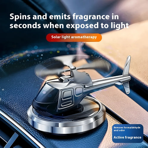 Silver metal solar-powered helicopter car air freshener rotating on a car dashboard.