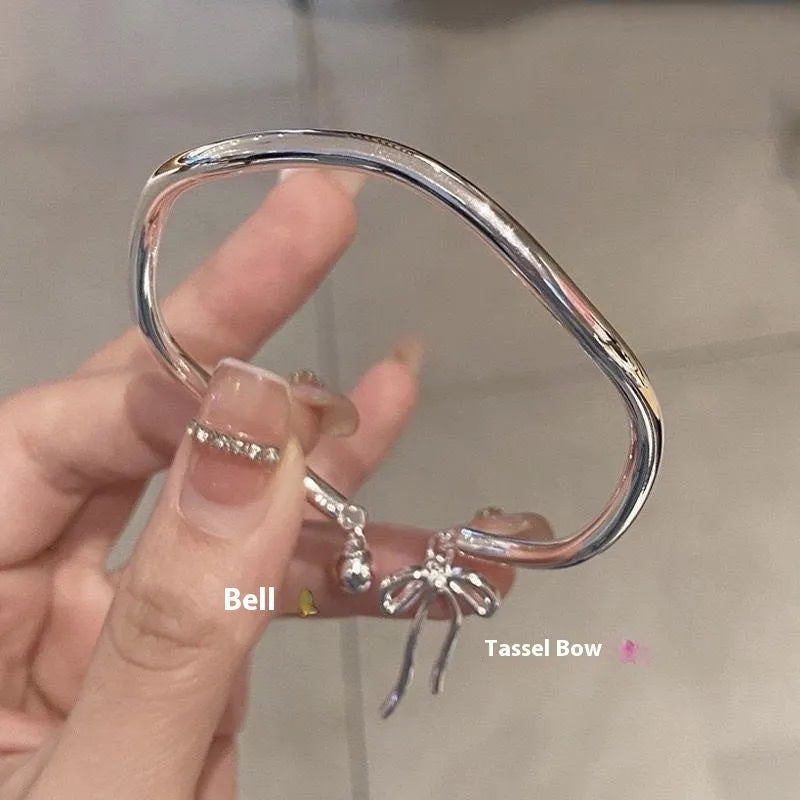 Silver tone adjustable bangle bracelet with a decorative bow charm and lobster clasp on a white background.