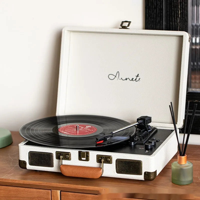 Cream-coloured retro phonograph in leather-effect suitcase with record on turntable and handle visible