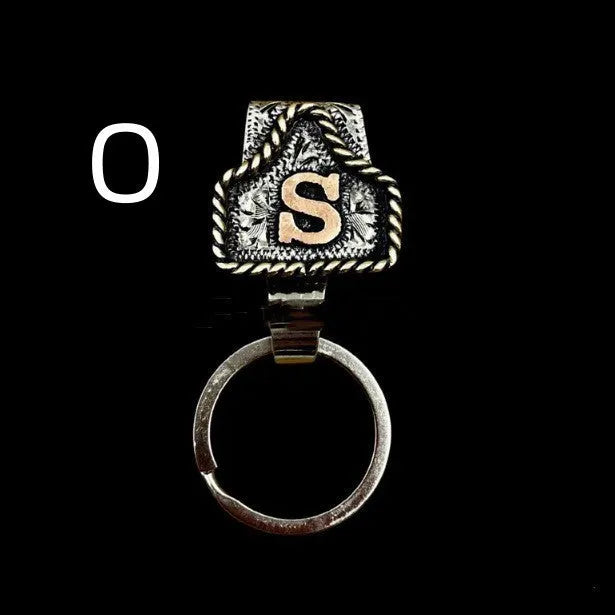 Handmade metal cow tag belt keychain showing one of 26 colour options, each marked with a different alphabet letter.