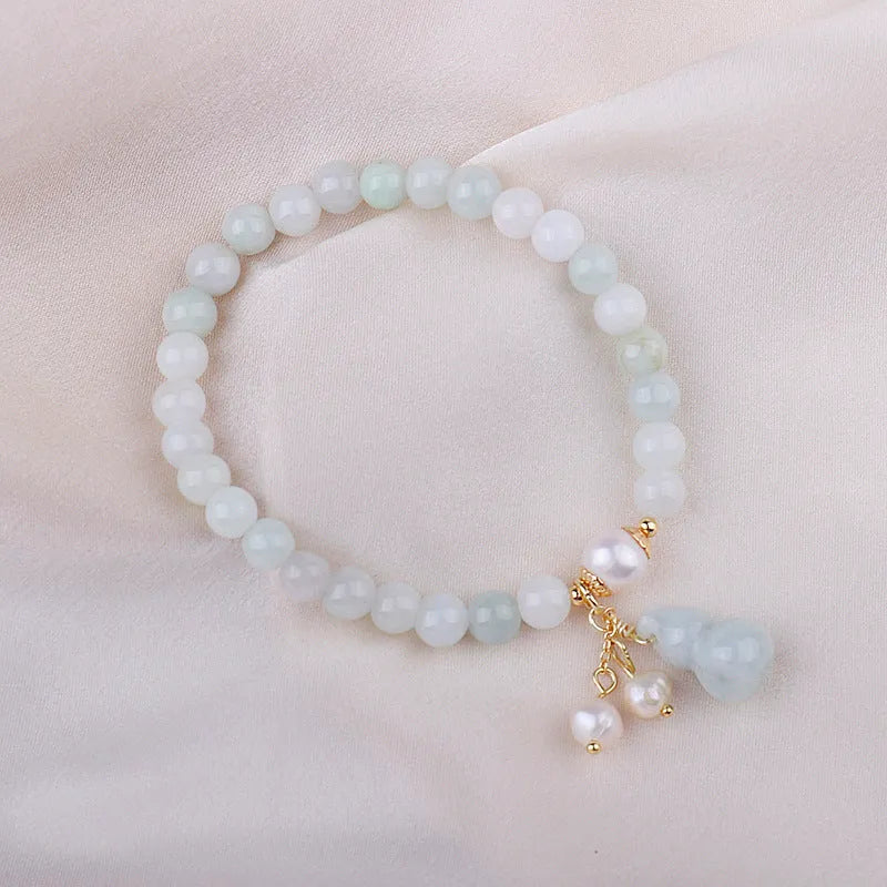 Close-up of a handmade emerald green jade gourd charm bracelet with a pearl detail on an adjustable cord.