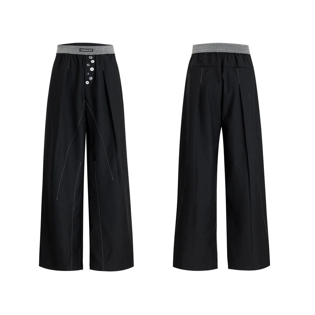 Straight-leg high-waisted trousers in black with a drooping waistband and button detail on a neutral background.