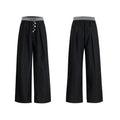 Straight-leg high-waisted trousers in black with a drooping waistband and button detail on a neutral background.