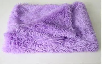 Soft grey long plush pet blanket for dogs on a wooden floor next to a kennel.