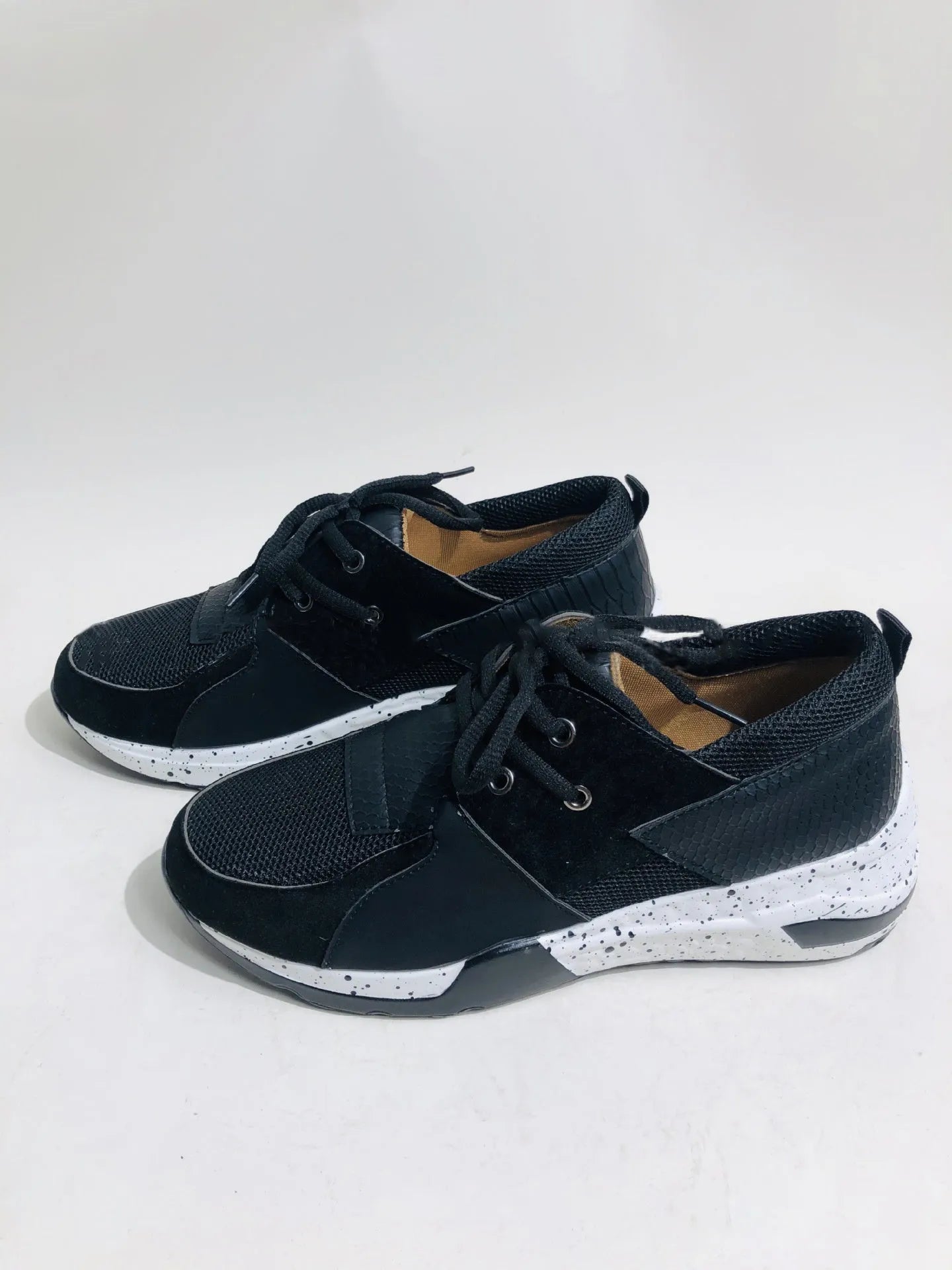 Women's black suede casual sneakers with a low wedge heel on a wooden floor.