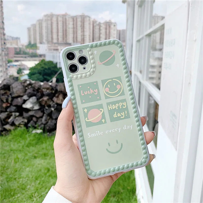 Green TPU iPhone case with geometric smiley face and polka dot pattern on a table.