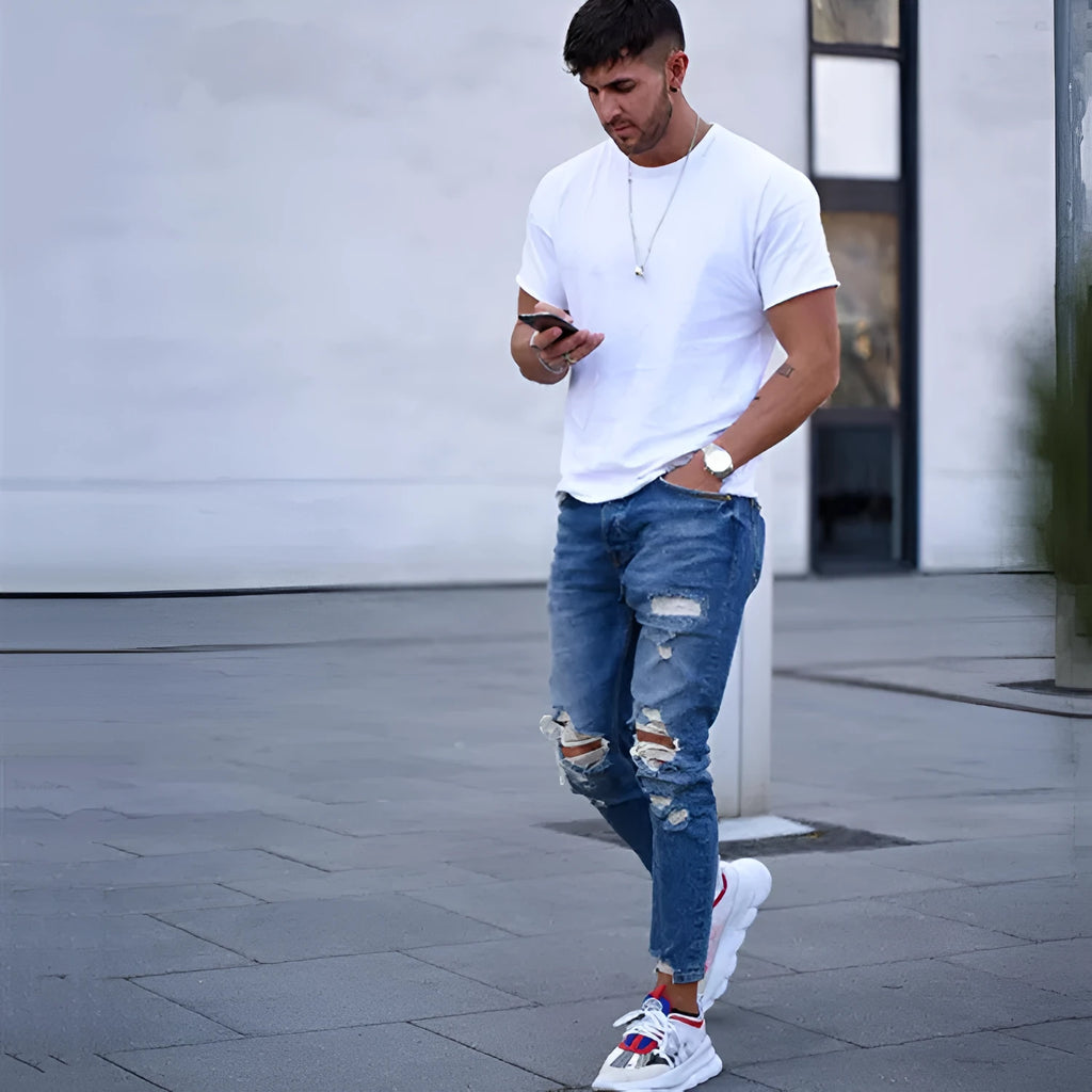 Men's deep blue cotton jeans with distressed hole detailing laid flat.