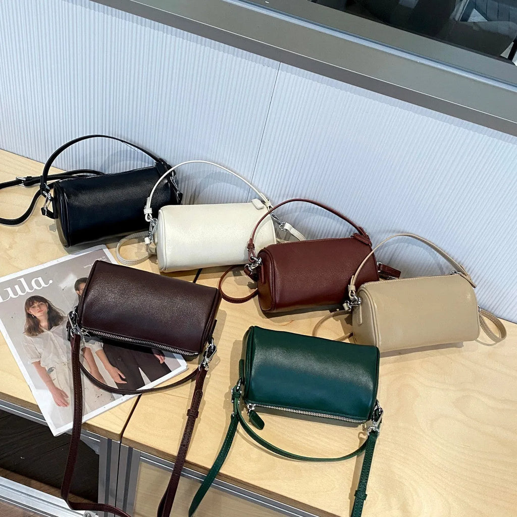Genuine leather cylindrical crossbody phone bag in black, shown with single shoulder strap and visible sewing thread detail.