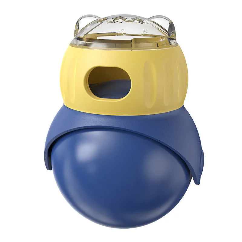 Yellow and blue owl-shaped plastic tumbler toy for cats, a slow-feeder puzzle on a wooden floor.