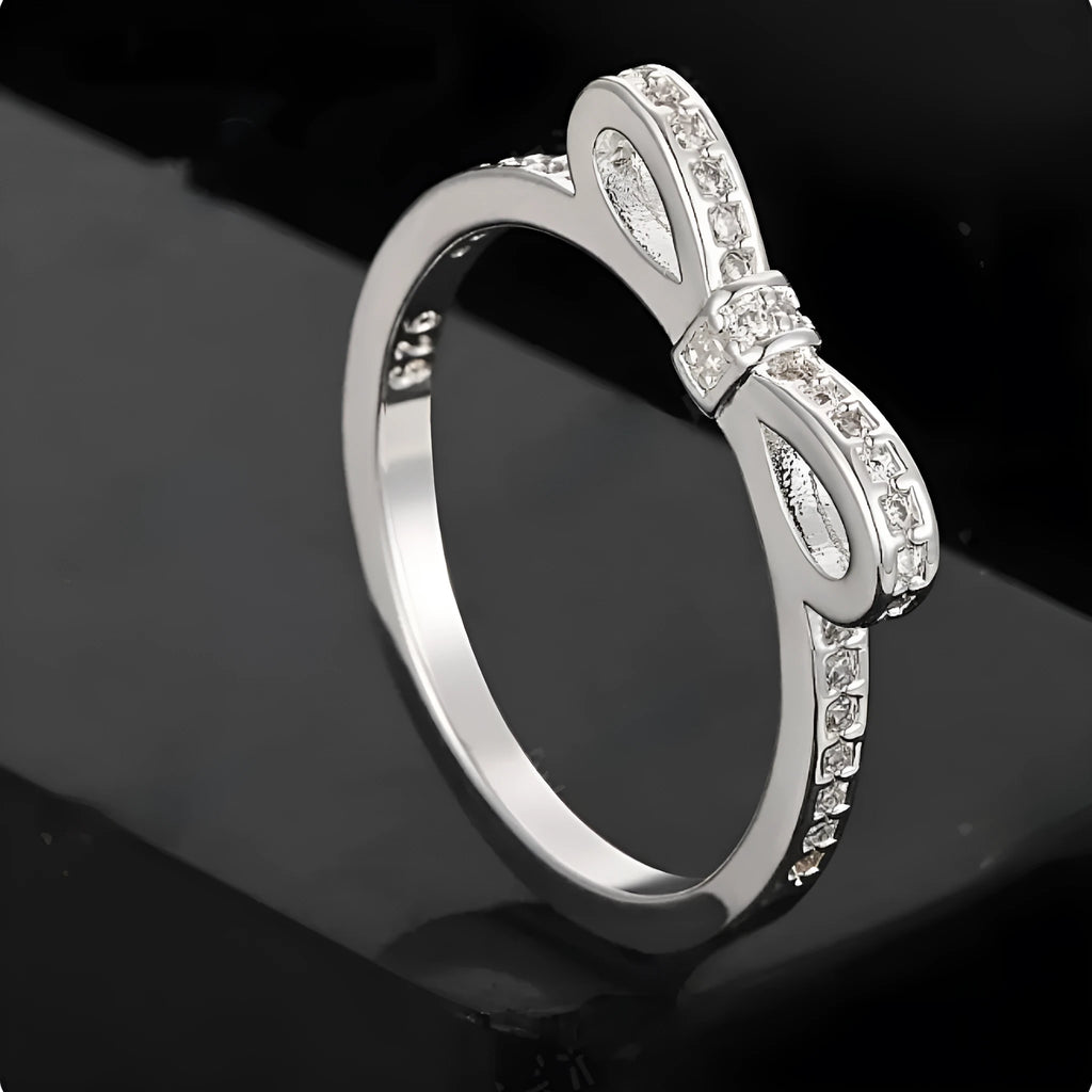 Silver-coloured bow-shaped ring with sparkling zircon crystals on a model's finger.