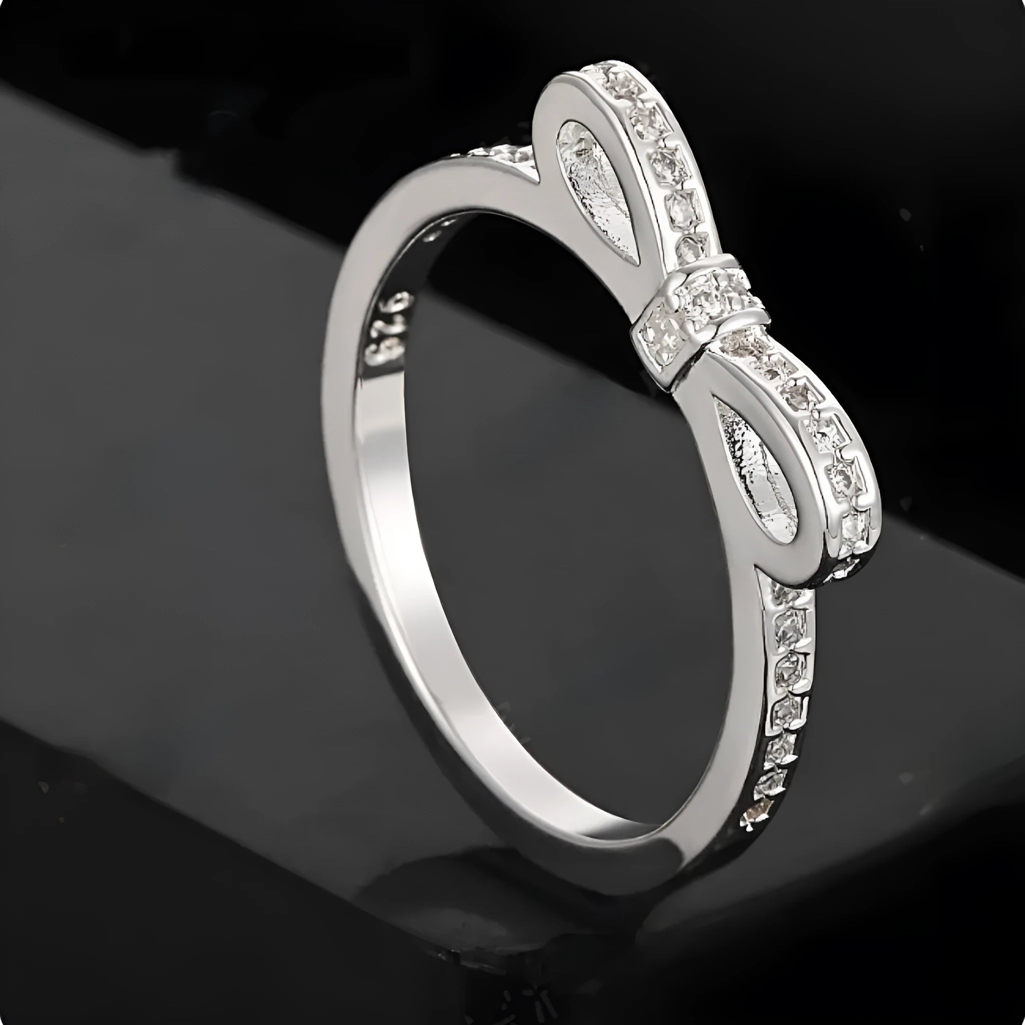 Silver-coloured bow-shaped ring with sparkling zircon crystals on a model's finger.