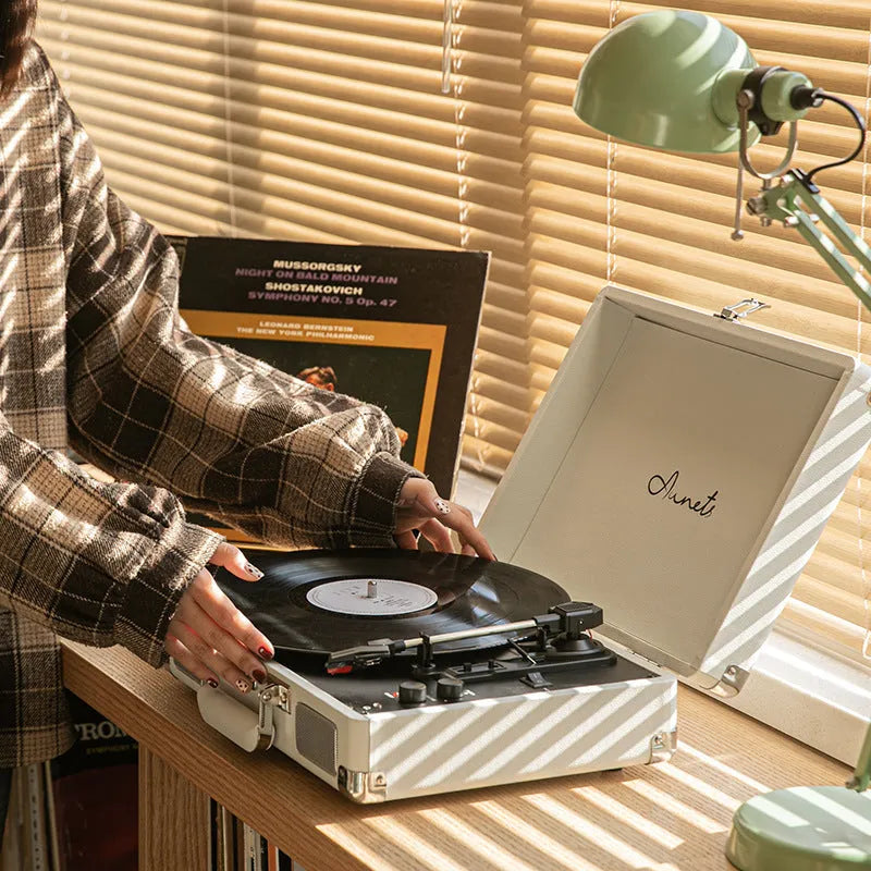 Cream-coloured retro phonograph in leather-effect suitcase with record on turntable and handle visible