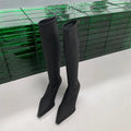 Black pointed toe below-the-knee women's boots with a stiletto heel and a visible back zipper on a plain background.
