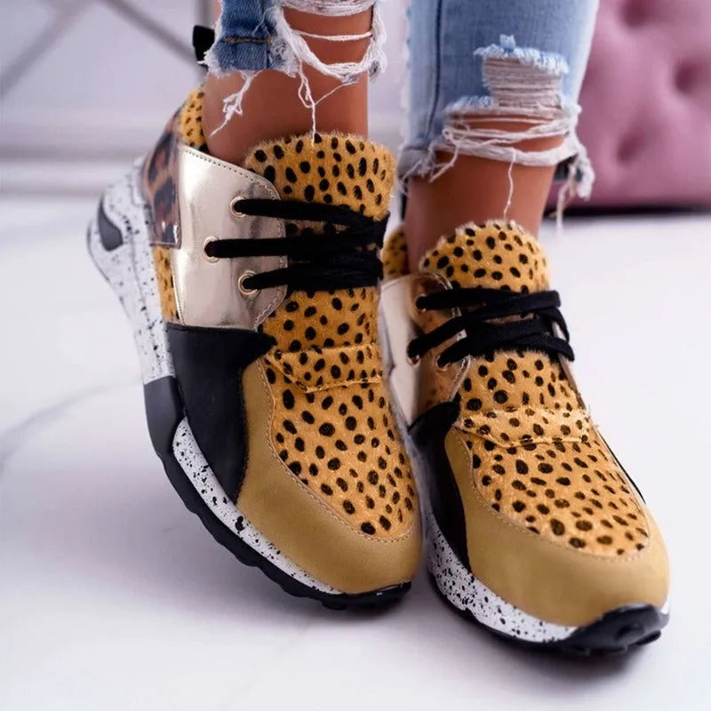 Women's black suede casual sneakers with a low wedge heel on a wooden floor.