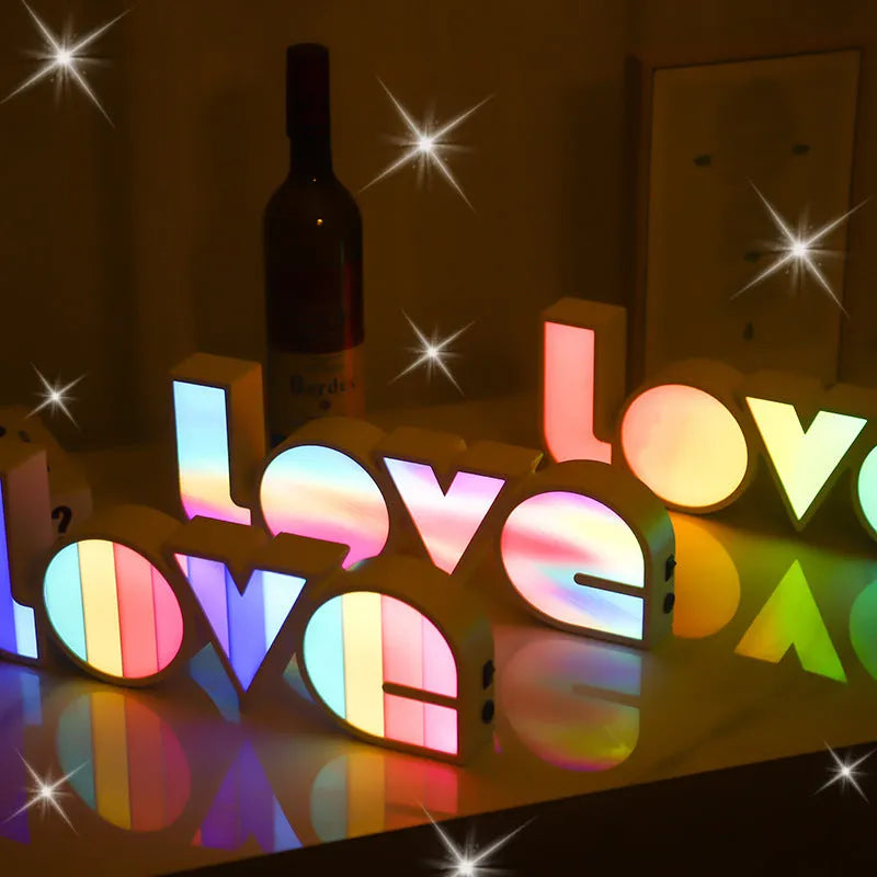 Rainbow-coloured LED LOVE decorative lamp with plastic shell on a table.