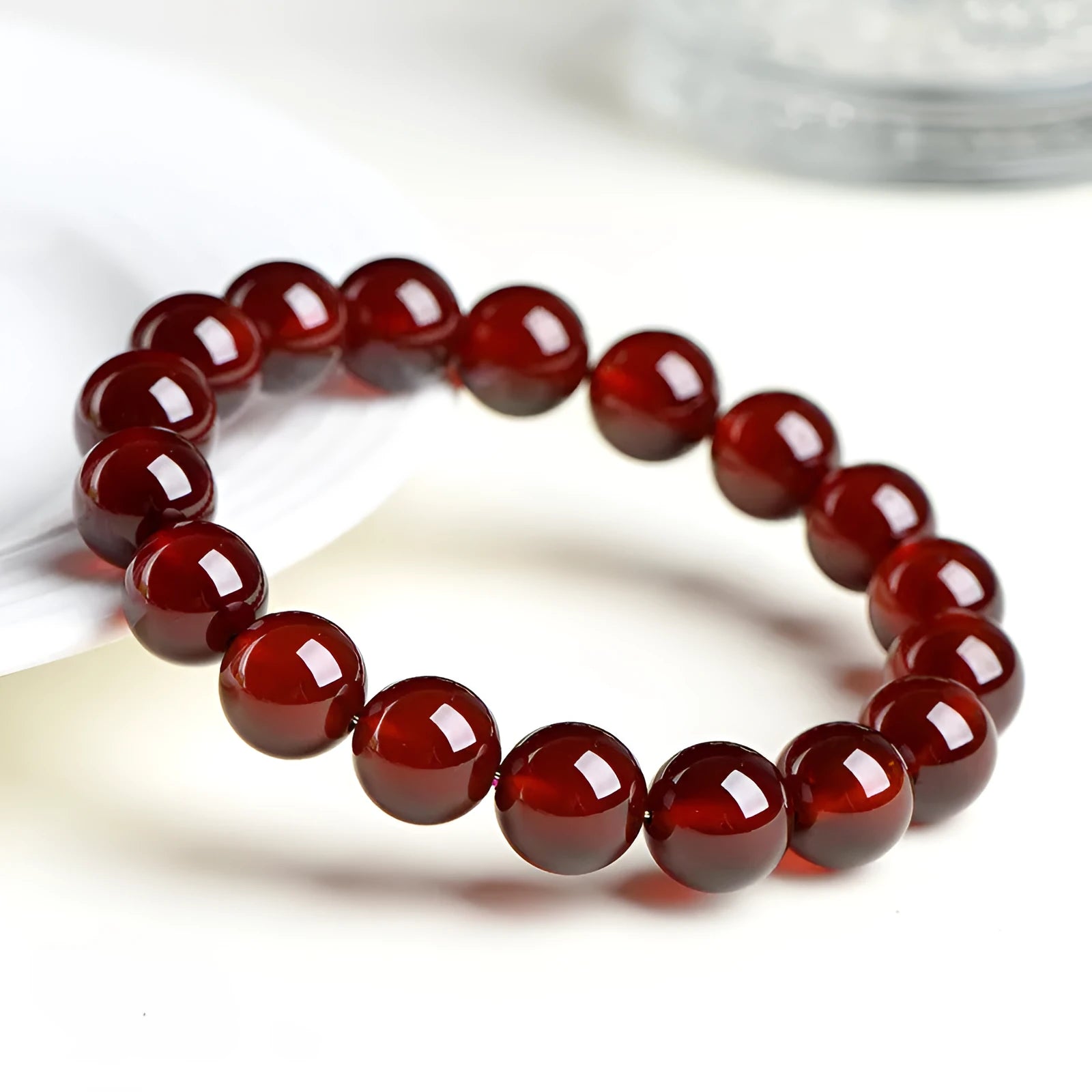 Natural orange red garnet crystal ball bracelet with a gold-toned Ruyi charm on a white background.