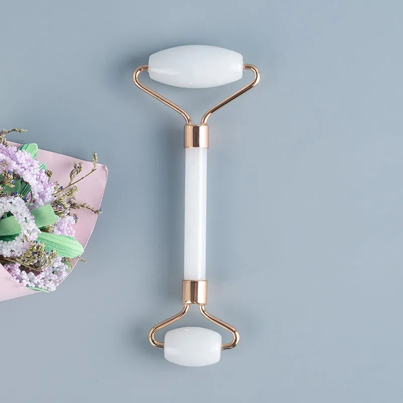 Natural white jade facial roller and gua sha scraper board set on a plain background.