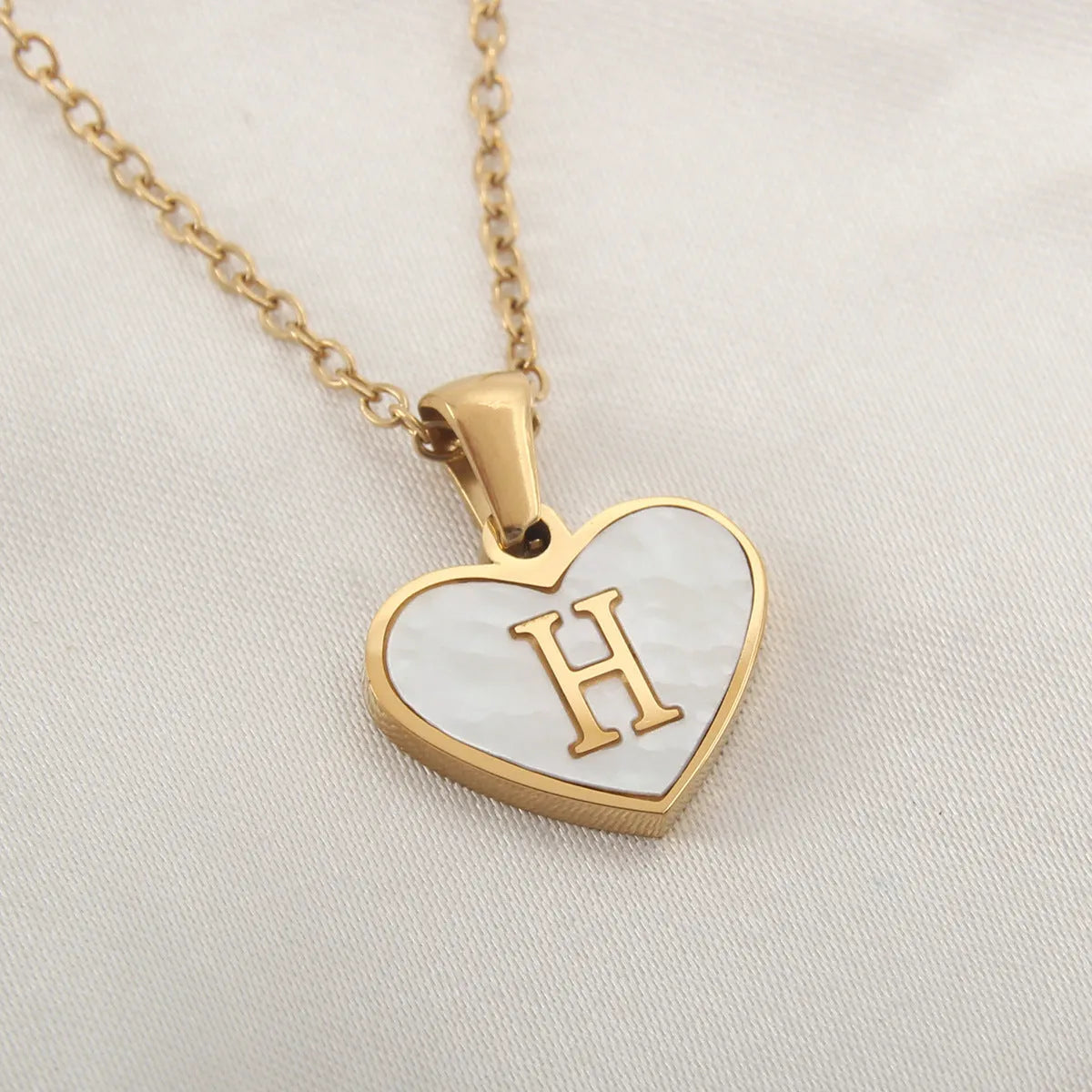 Gold-plated heart necklace with white shell pendant showing initial engraving on stainless steel chain