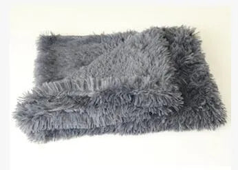 Soft grey long plush pet blanket for dogs on a wooden floor next to a kennel.