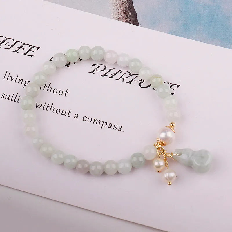 Close-up of a handmade emerald green jade gourd charm bracelet with a pearl detail on an adjustable cord.