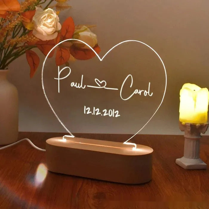 Custom transparent acrylic night light with engraved names and date, lit by an LED base on a table.